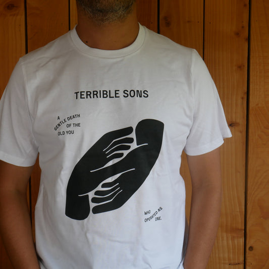 Man wearing a white ‘ gentle death t shirt’ close up against a wooden wall