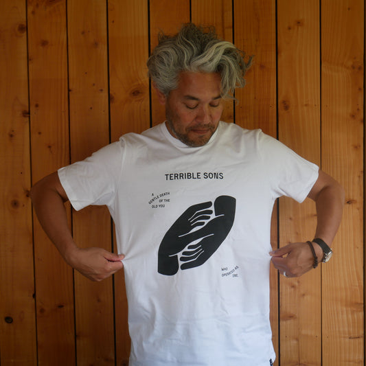 Man wearing a white ‘ gentle death’ t shirt against a wooden wall back ground.